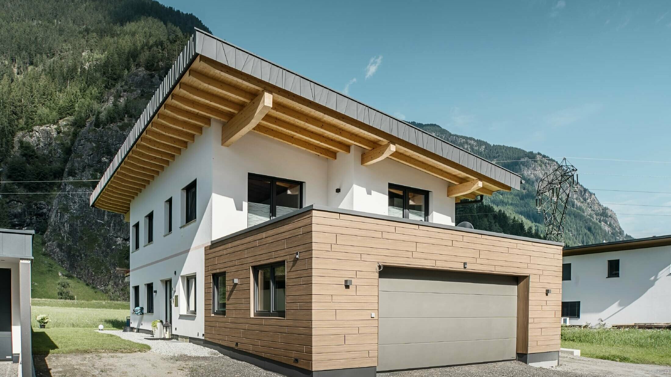 Ett bostadshusgarage med PREFA-fasadpaneler i trälook med färgton ”valnötsbrun”. Bakgrunden bjuder på utsikt över berg.. 