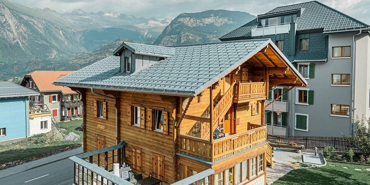 Traditionell schweizisk trästuga med takkupa och sadeltak. Taket är täckt med de klassiska takpannorna från PREFA i stengrått.