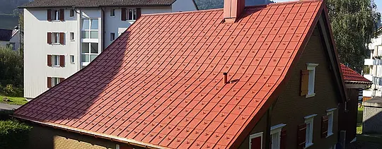 Sadeltak täckt med PREFA-takplattor av aluminium. Tak i tegelrött med snöstoppare och skorsten