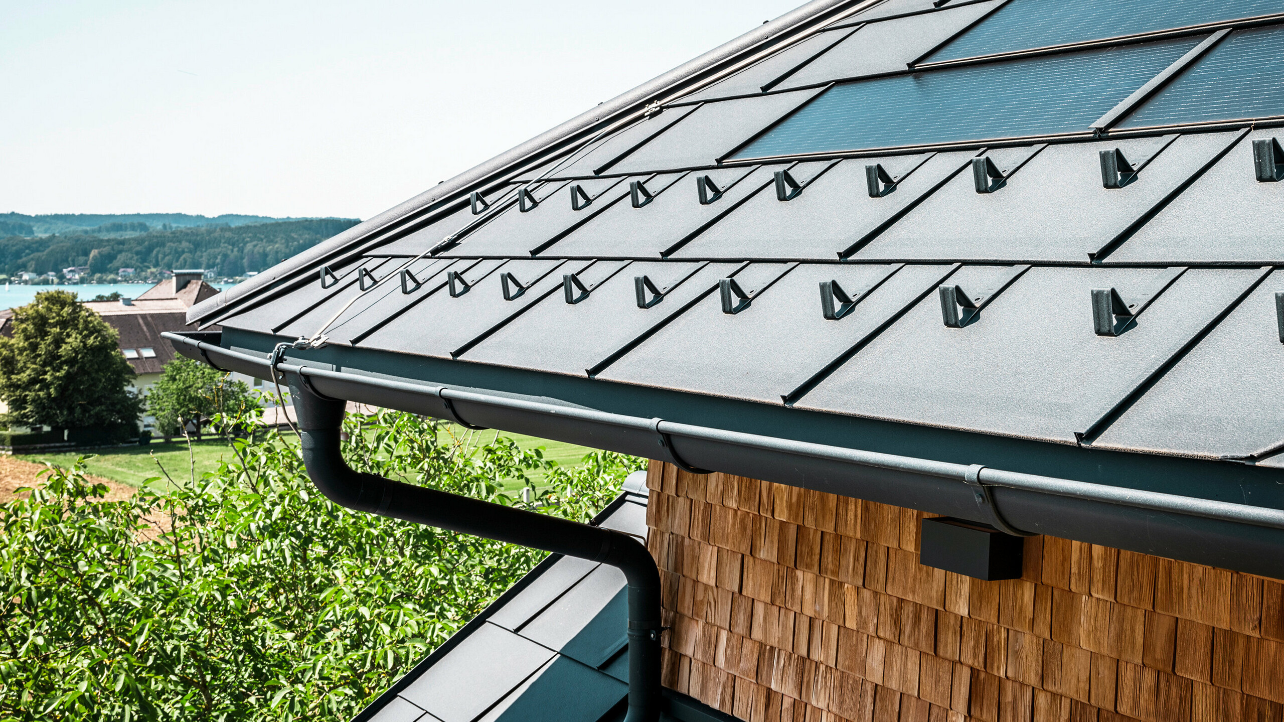 Zenz'n Stub'n i Schörfling am Attersee har fått ett nyrenoverat tak med innovativa PREFA soltakplattor och hållbara PREFA Takplatta R.16 i P.10 antracit. Det stilrena aluminiumtaket kombinerar modern design med hållbar energiutvinning. Takavvattningen, som består av avloppsrör och hängränna i P.10 antracit, smälter harmoniskt in i helhetsbilden och understryker den högkvalitativa utförandet. I bakgrunden glittrar Attersees blå vatten.