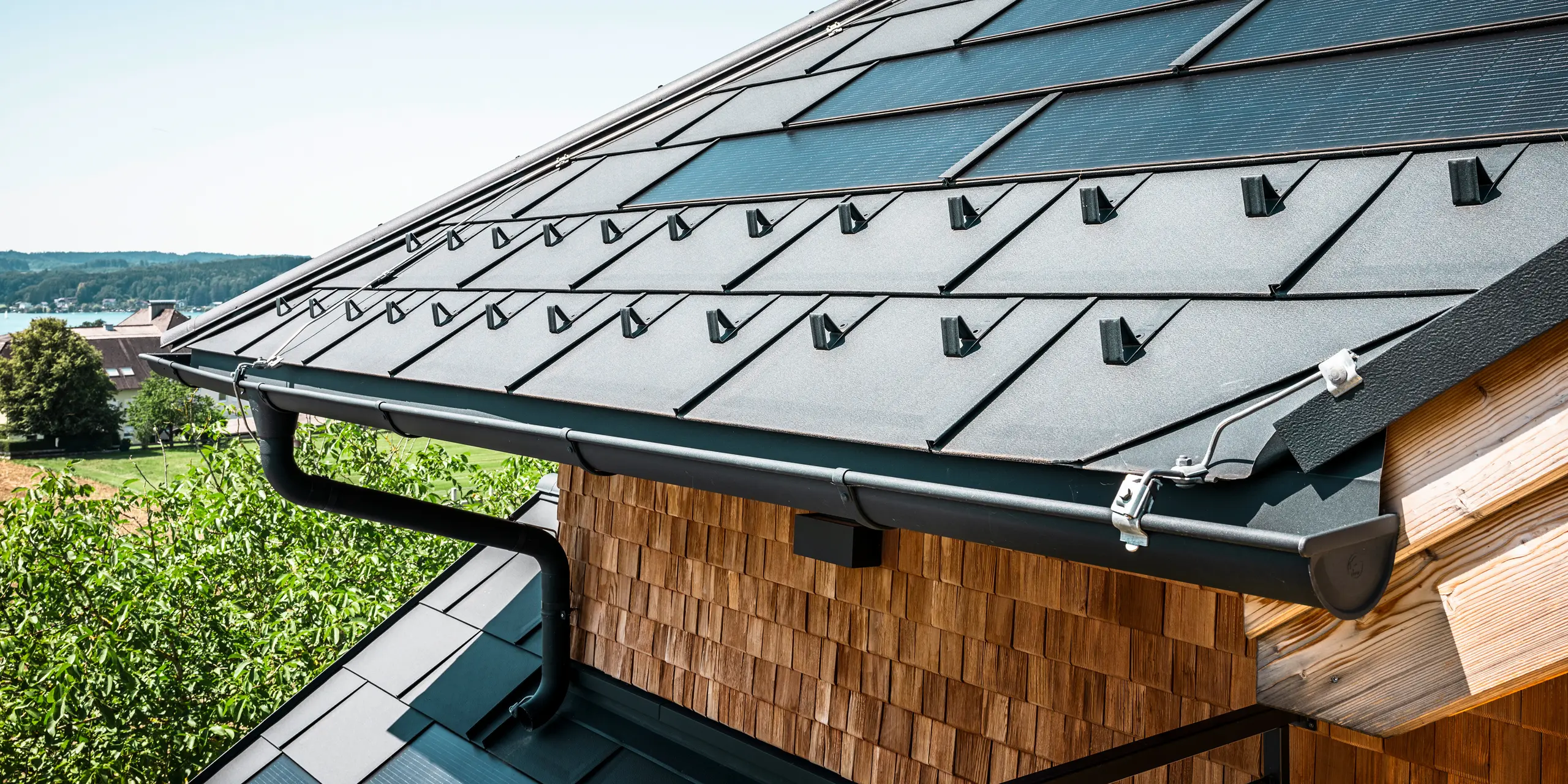 Zenz'n Stub'n i Schörfling am Attersee har fått ett nyrenoverat tak med innovativa PREFA soltakplattor och hållbara PREFA Takplatta R.16 i P.10 antracit. Det stilrena aluminiumtaket kombinerar modern design med hållbar energiutvinning. Takavvattningen, som består av avloppsrör och hängränna i P.10 antracit, smälter harmoniskt in i helhetsbilden och understryker den högkvalitativa utförandet. I bakgrunden glittrar Attersees blå vatten.