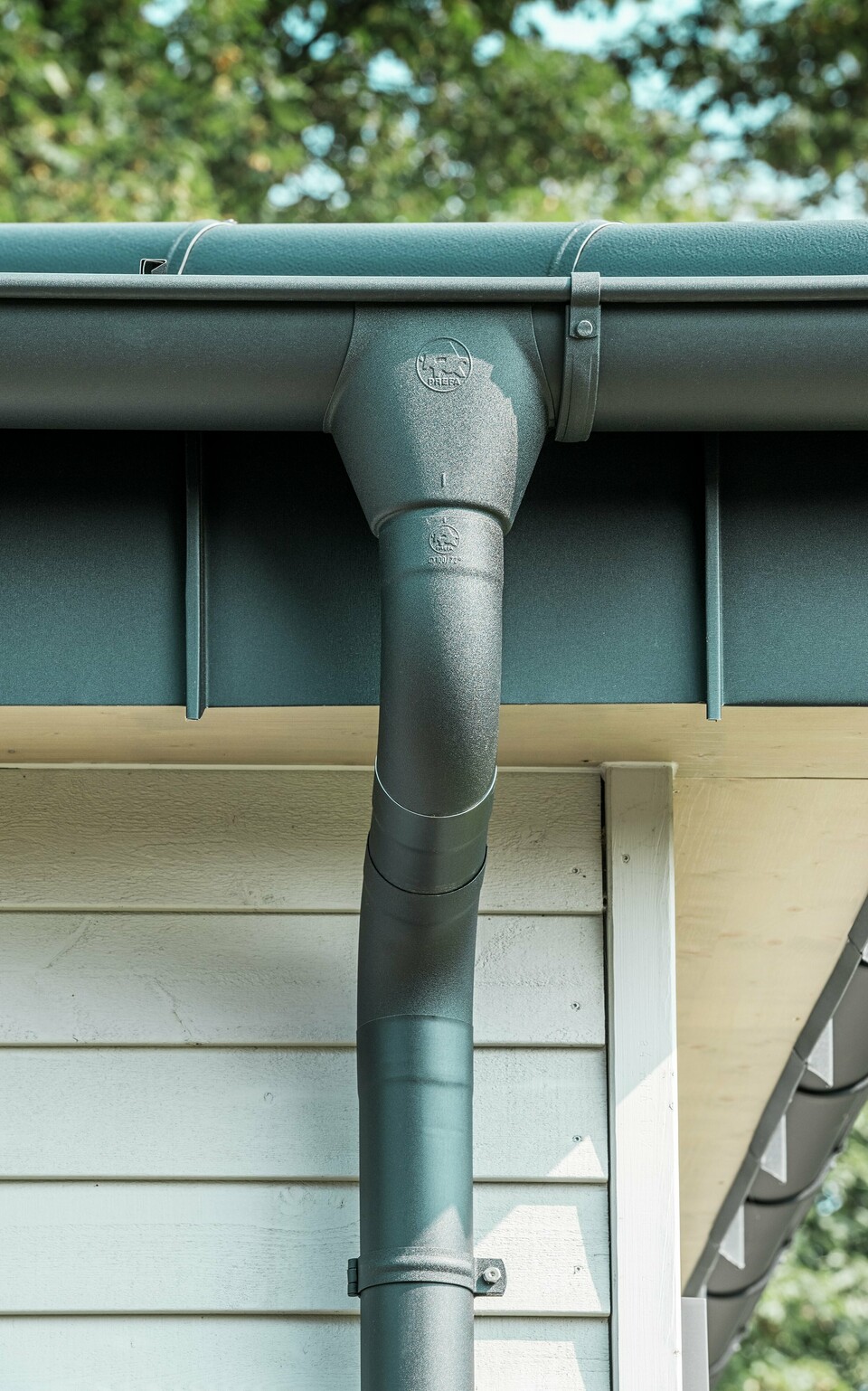 Nahaufnahme der robusten PREFA Dachentwässerung eines Bungalows in Rommerskirchen. Die hochwertige Saumrinne und das Ablaufrohr in P.10 Schwarz bieten optimalen Schutz vor Witterungseinflüssen. Langlebigkeit und Funktionalität verbinden sich hier mit elegantem Design aus Aluminium.