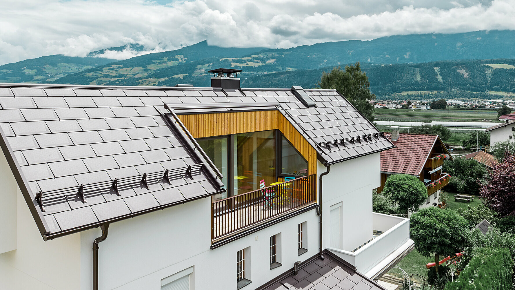 Bostadshus med ljus putsfasad, stor balkong och taktäckning med PREFAs takplattor R.16 i färgen nötbrun.