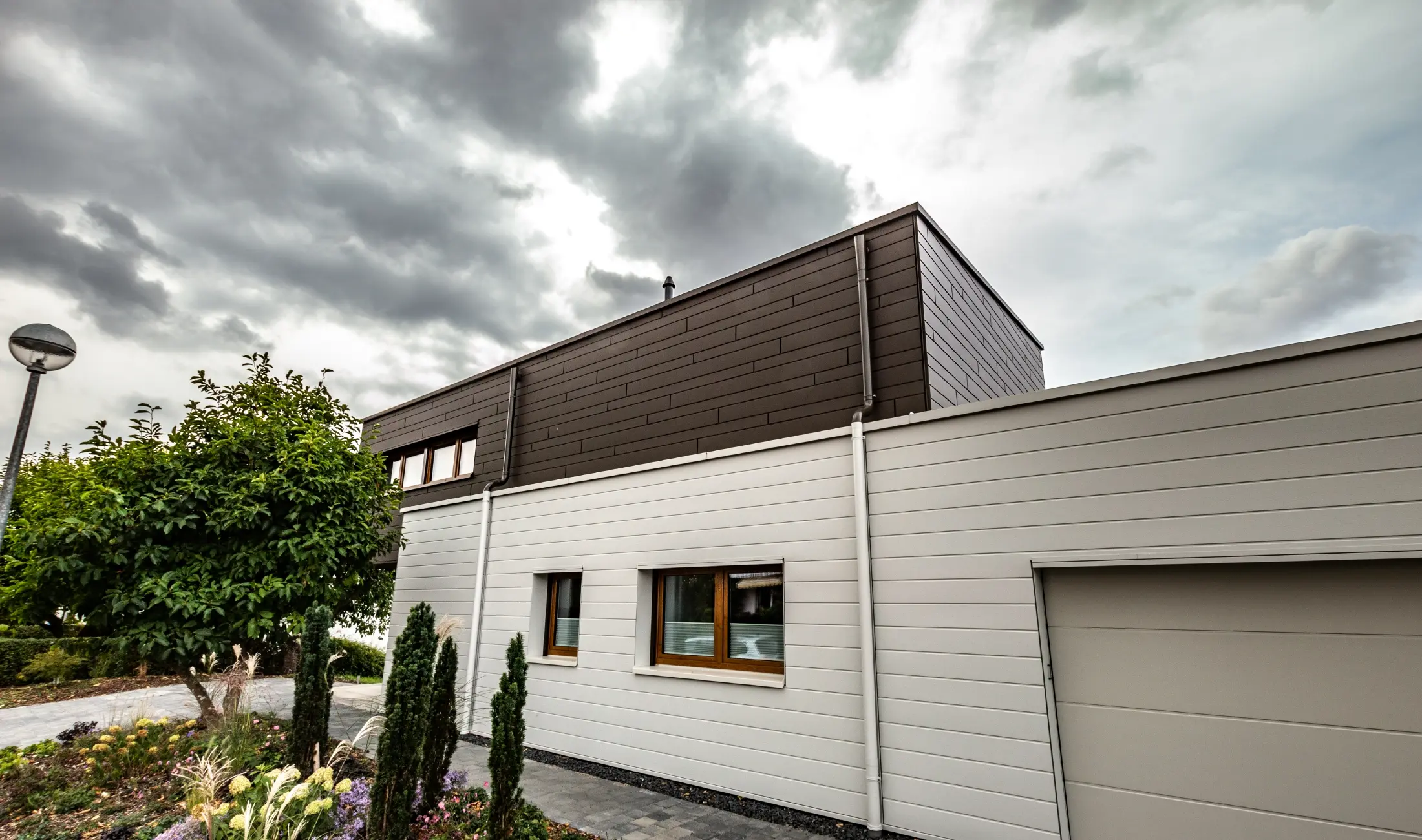 Fasadbeklädnad av ett garage med PREFA fasadpaneler, horisontella i vitt, med vägganslutning till avvattningssystem.