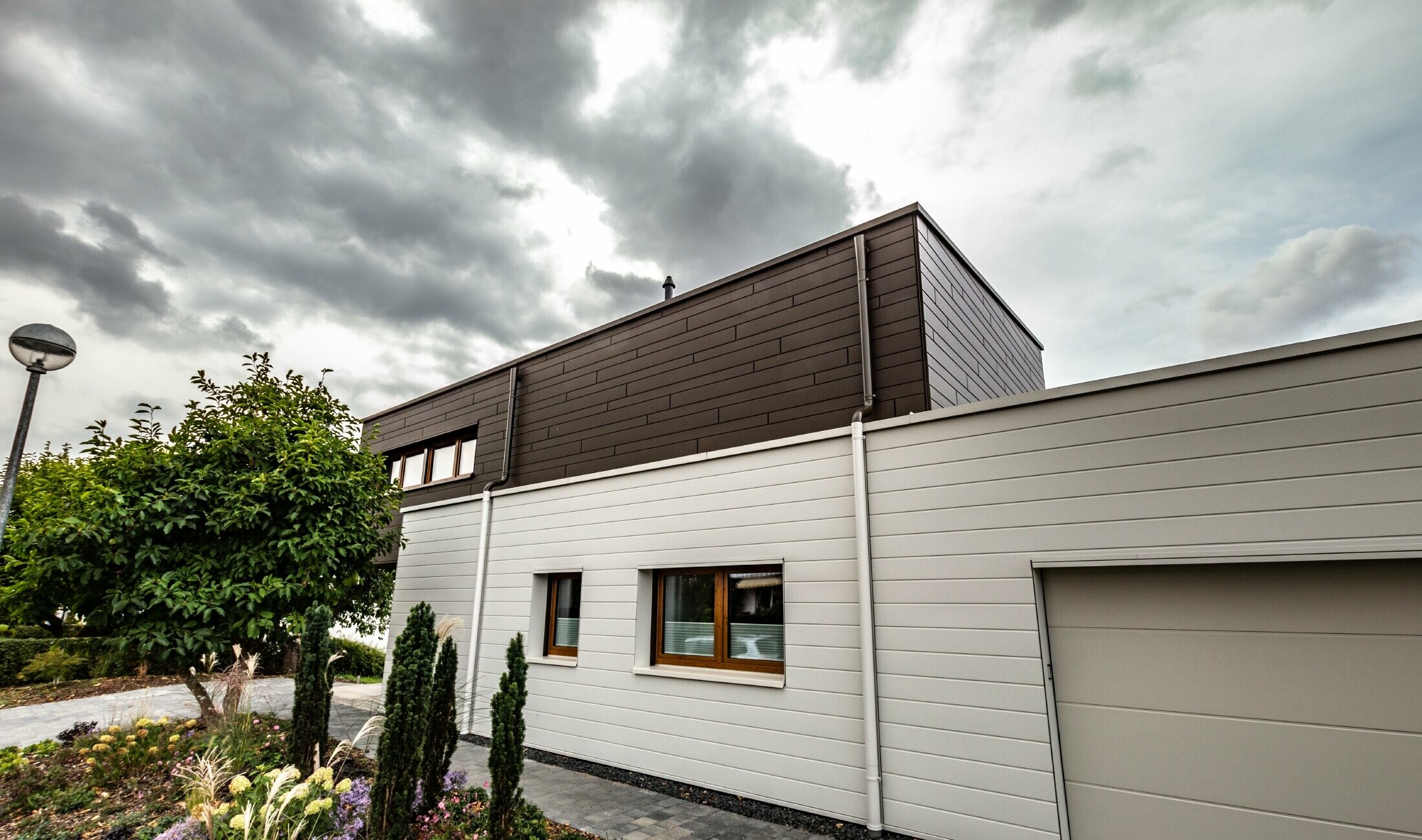Fasadbeklädnad av ett garage med PREFA fasadpaneler, horisontella i vitt, med vägganslutning till avvattningssystem.
