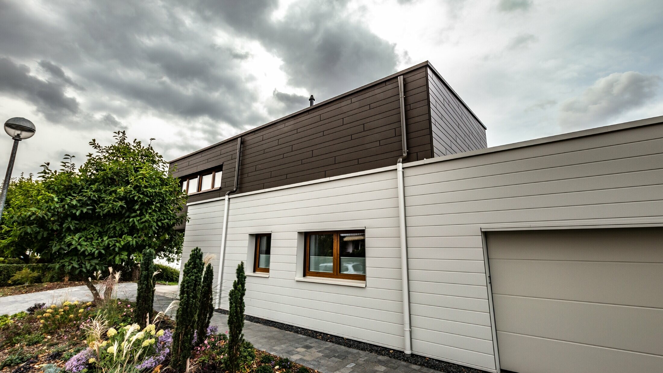 Fasadbeklädnad av ett garage med PREFA fasadpaneler, horisontella i vitt, med vägganslutning till avvattningssystem.