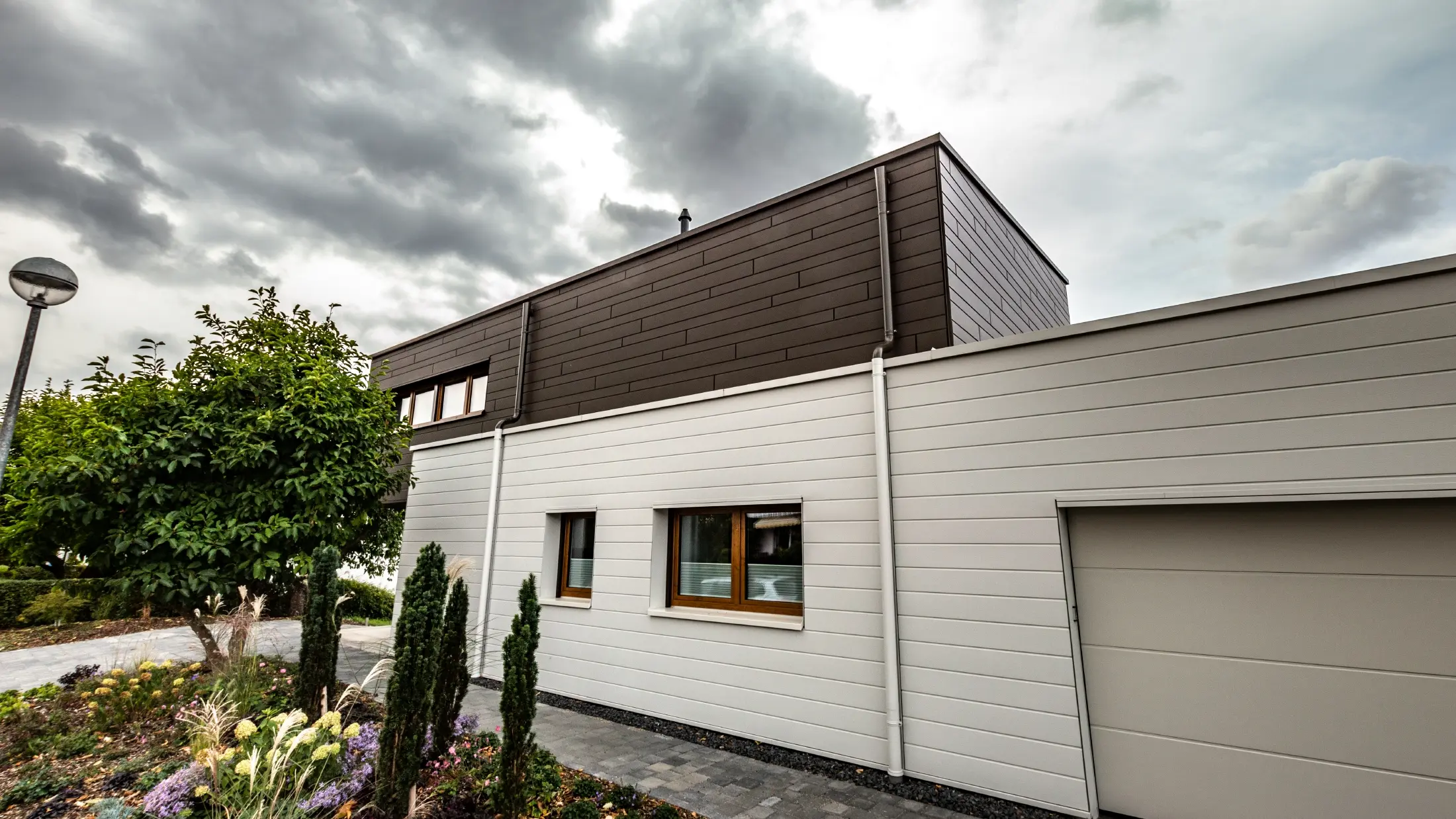 Fasadbeklädnad av ett garage med PREFA fasadpaneler, horisontella i vitt, med vägganslutning till avvattningssystem.