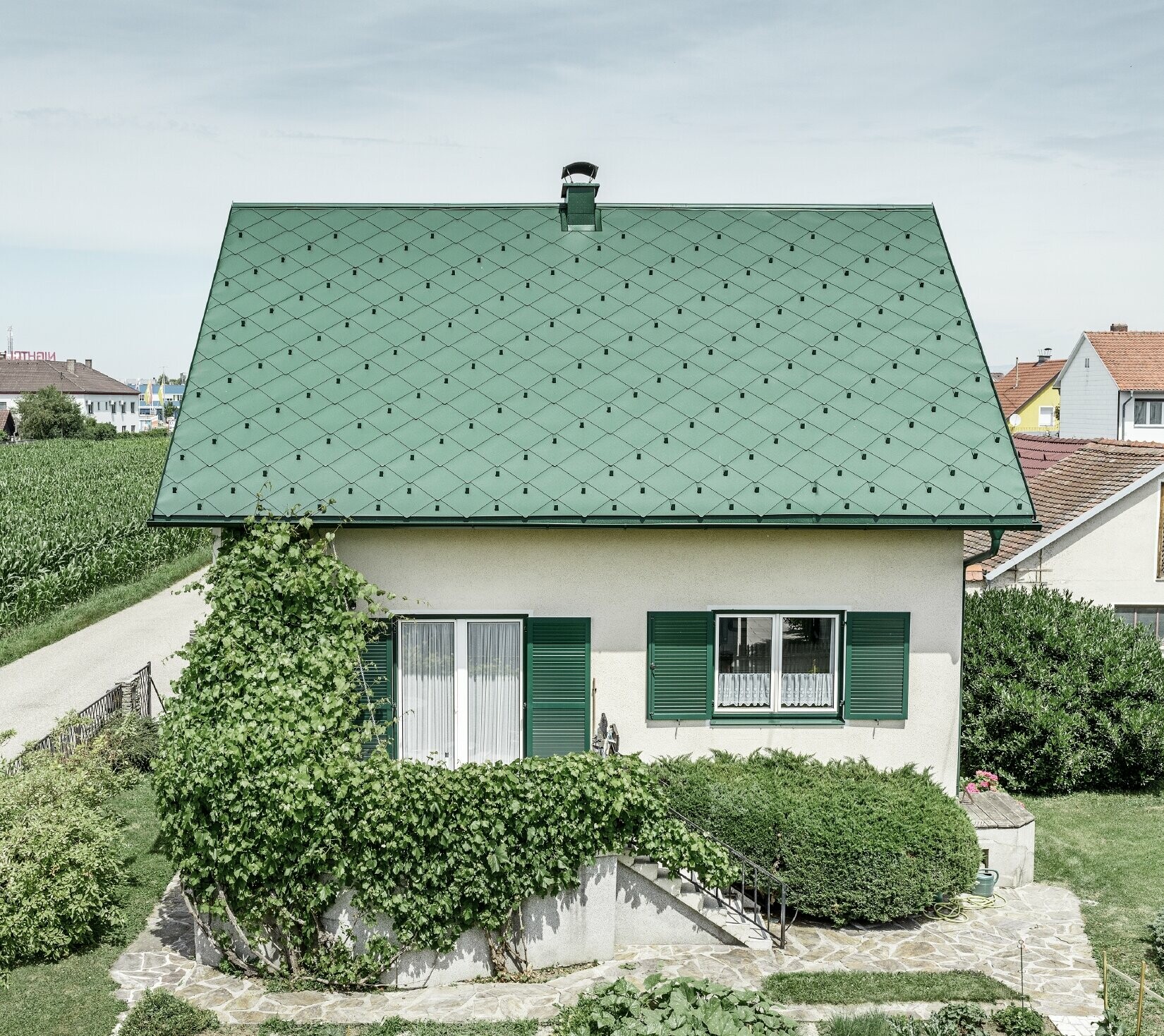 Klassiskt enfamiljshus med sadeltak med en taktäckning av aluminium i mossgrön med gröna fönsterluckor Taket täcktes med PREFA takromber 44 × 44 i P.10 mossgrön.