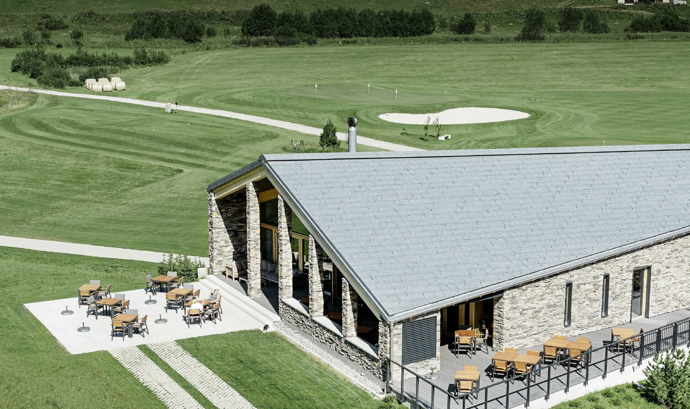 Modernt klubbhus vid golfbanan i Andermatt med stenfasad och PREFA:s takpanel FX.12 av aluminium i stengrått