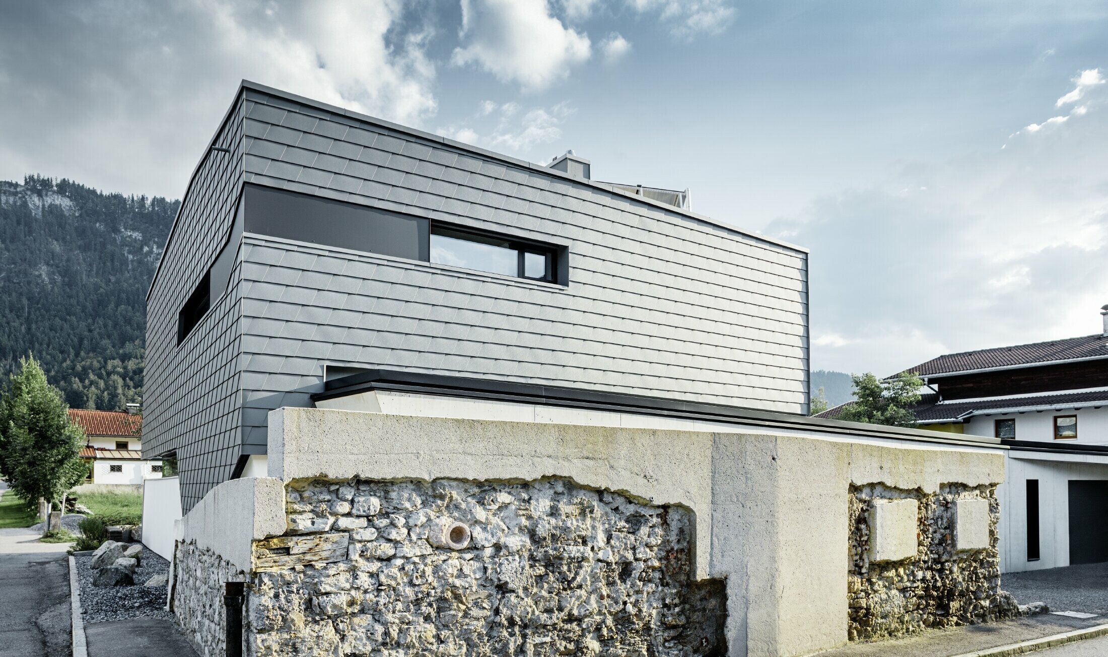 modernt enfamiljshus med plantak, stora fönsterytor och en ljusgrå shingelfasad av aluminium från PREFA