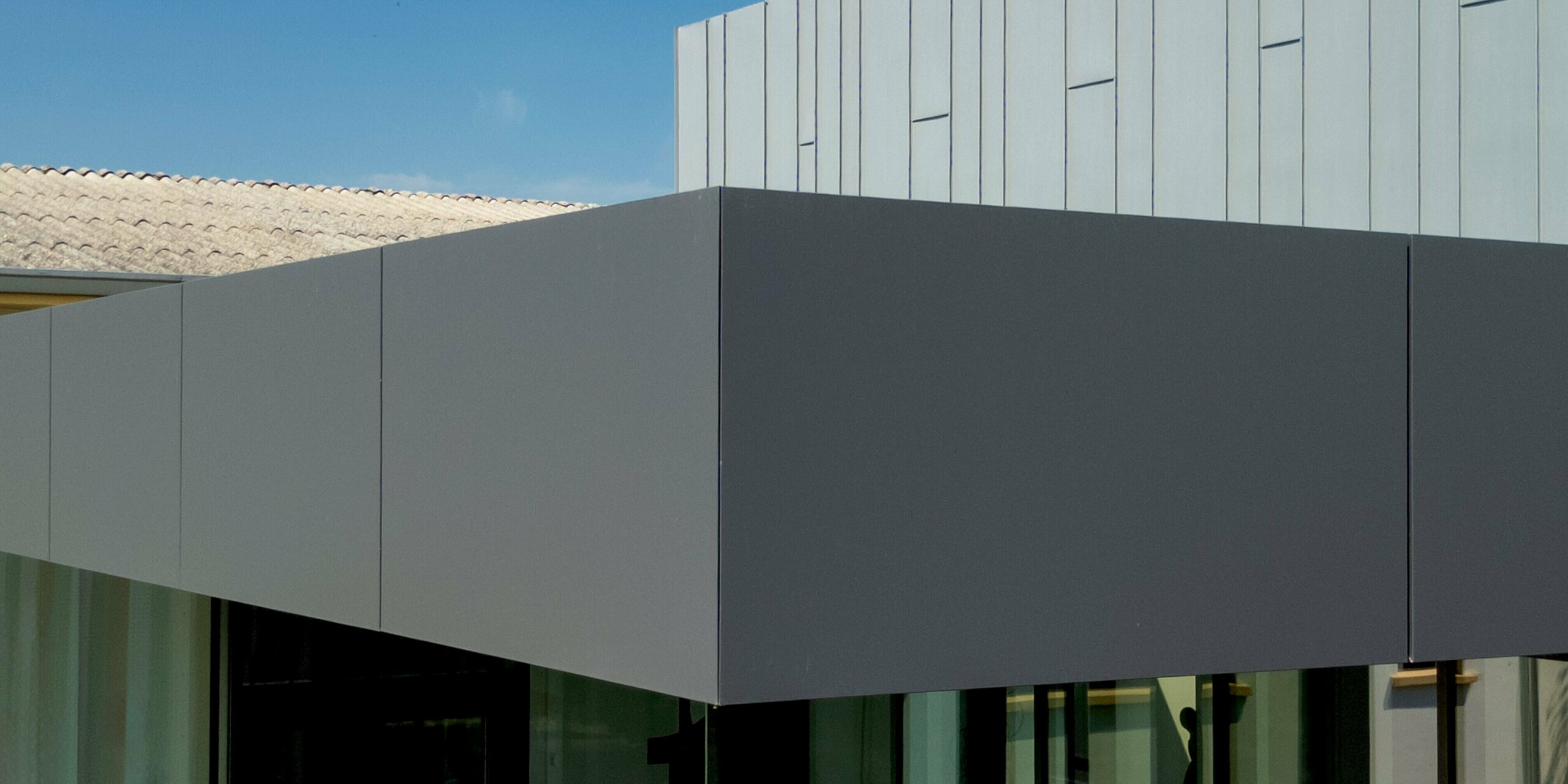 Präzision trifft Eleganz: Ein markanter Gebäudevorsprung in sattem Dunkelgrau schwebt scheinbar schwerelos über einer raumhohen Glasfassade – ein architektonisches Highlight der Scuola Arte e Mestieri F. Bertazzoni in Suzzara. Der fließende Farbübergang vom dunkleren PREFABOND-Volumen zur vertikal gegliederten PREFALZ-Fassade in Patinagrau erzeugt eine fesselnde Tiefenwirkung. Die makellos verarbeiteten PREFA Aluminiumprodukte überzeugen mit präzisen Fugen, perfekter Formstabilität und langfristiger Witterungsbeständigkeit – modernes Bildungsdesign, das Qualität auf den ersten Blick sichtbar macht.