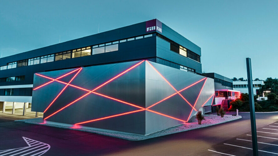 Fasad av en företagsbyggnad med en svängd vägg, som är klädd med PREFA kompositskiva av borstat aluminium.