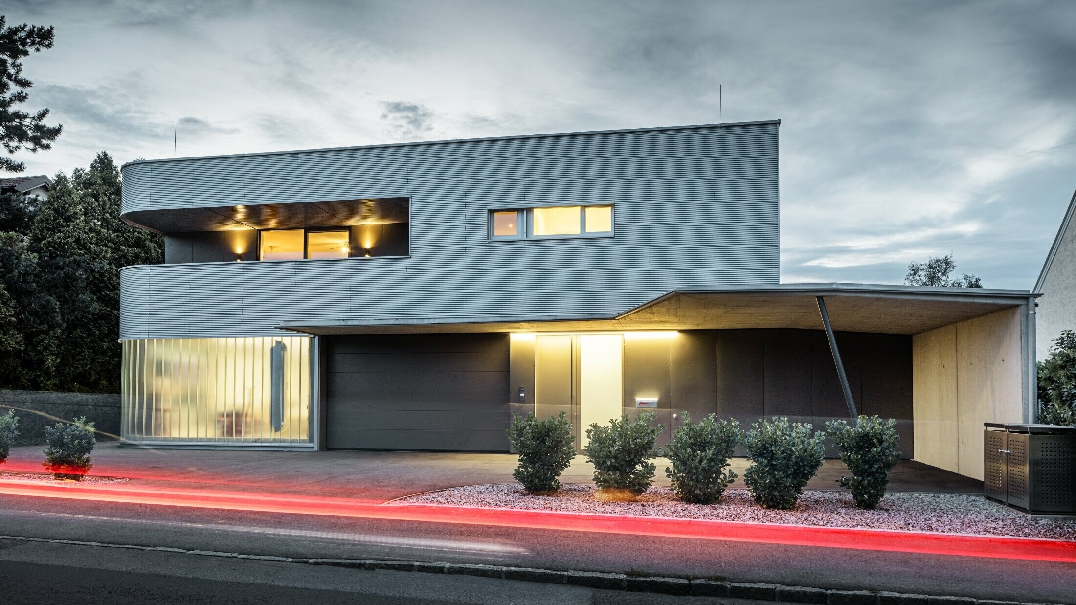 Modernt bostadshus med valsblank PREFA vågprofilsfasad, med garage, fotograferat i kvällsljus