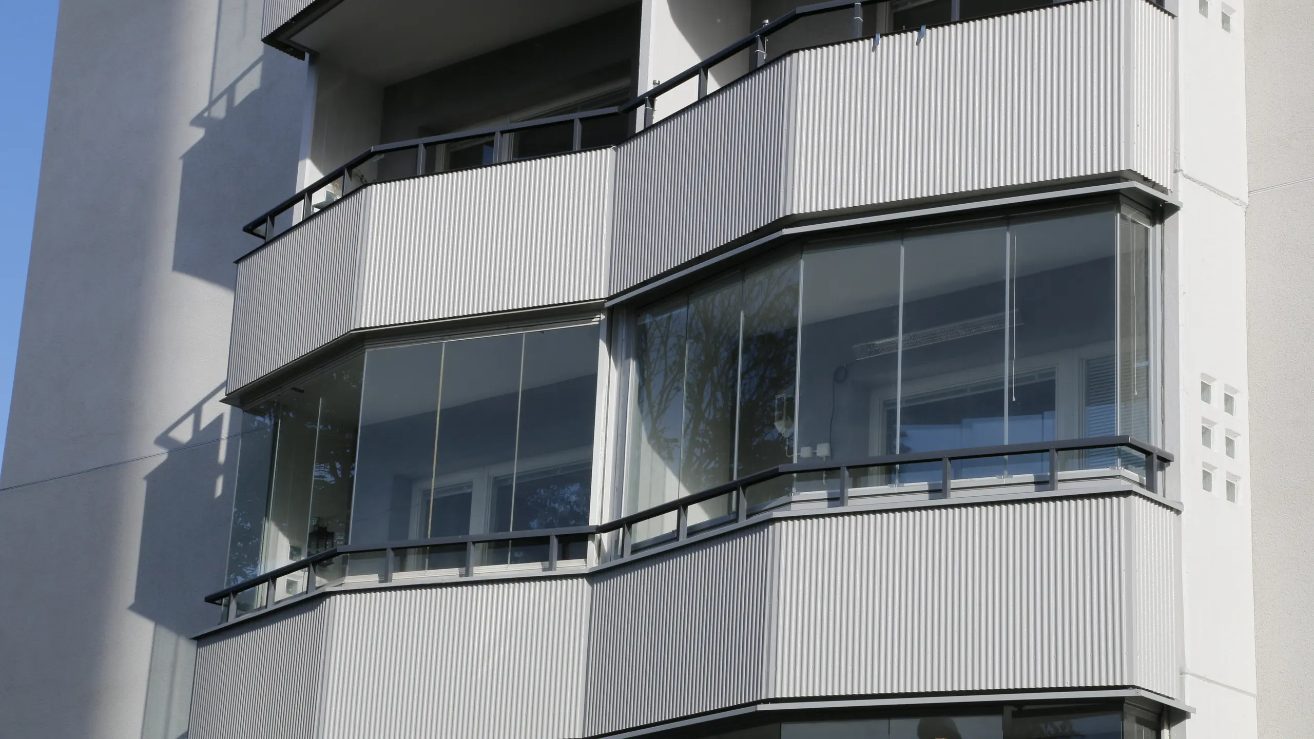 Inglasade balkonger med ljusgrå Alustucco-beklädnad i en ovanlig, vinklad form som ger fasaden ett eget uttryck.