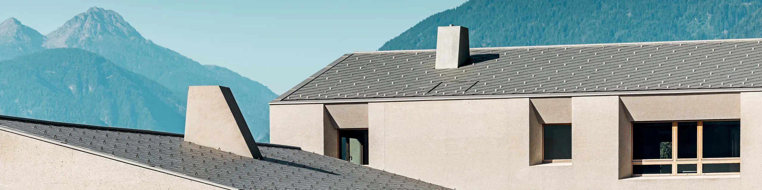Das Bildungszentrum Riffian in Südtirol setzt mit PREFA Dachrauten in der Größe 44 × 44 und der Farbe P.10 Bronze einen markanten Akzent vor alpiner Kulisse. Das präzise verlegte Aluminiumdach harmoniert mit der ruhigen, an Lehm erinnernden Fassade und unterstreicht die moderne Architektur von Kindergarten und Volksschule.