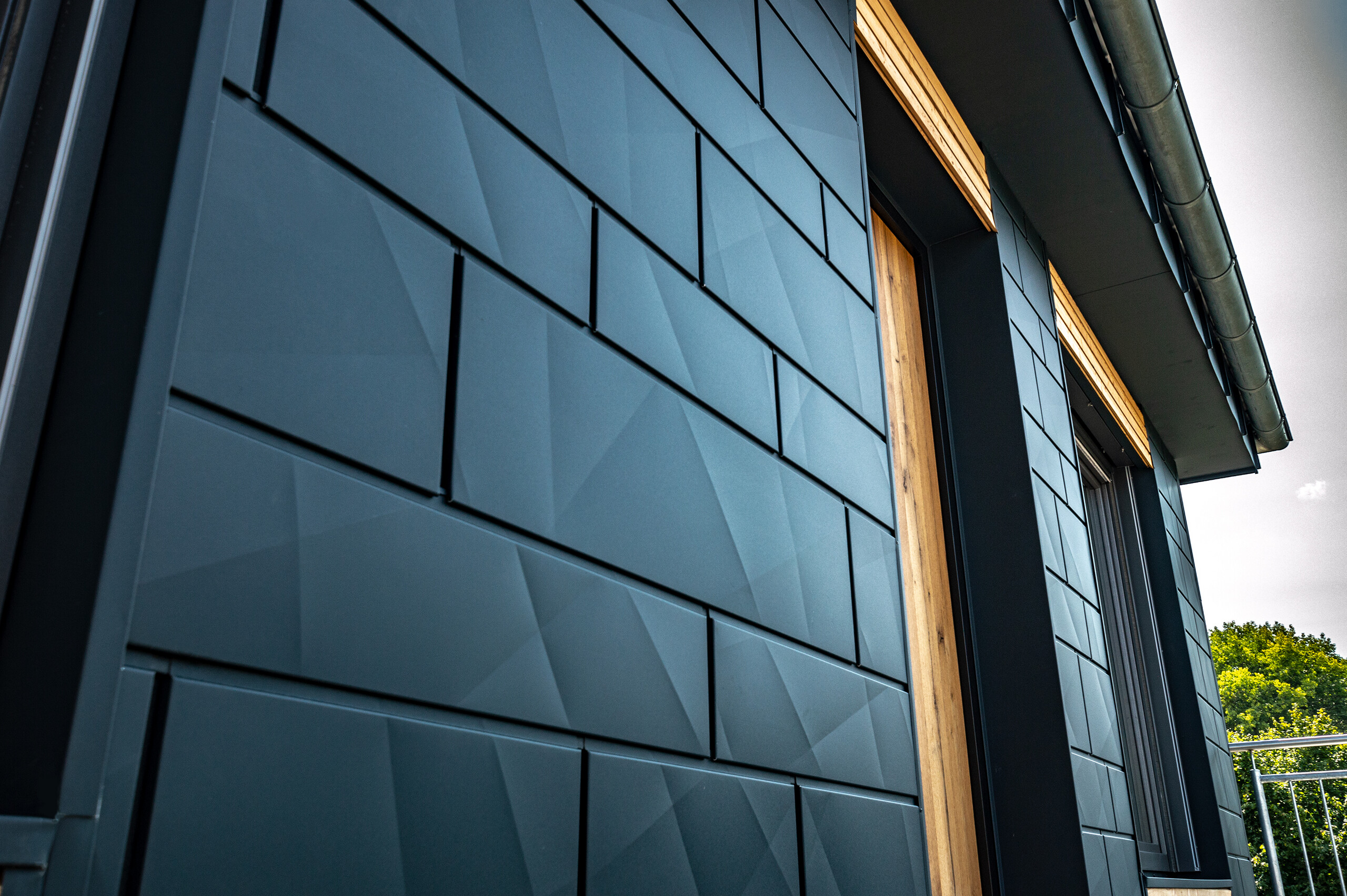 Fasad med PREFA Siding.X i antracit med balkongdörrar och stora glasytor blandat med en träfasad.