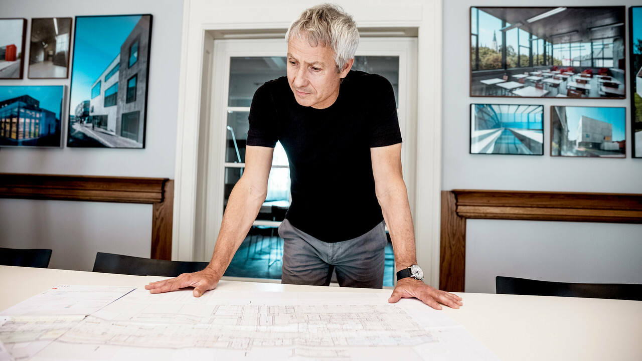 Arkitekten arbetar med detaljerade byggplaner i ett modernt kontor, omgiven av imponerande bilder från PREFA:s arkitekturprojekt.