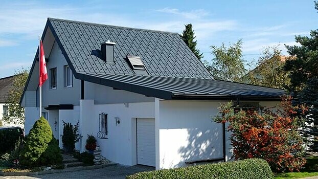 Renoverat hus med sadeltak och garage. Taket är täckt med PREFA takplatta och garaget med Prefalz i antracit. Framför huset finns en flaggstång med Schweiz flagga.