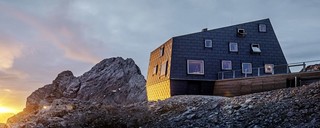 Vorderansicht der Schutzhütte am Dachstein vor einem atemberaubenden Sonnenuntergang, verkleidet mit PREFA Dach- und Fassadenpaneelen FX.12 in P10 Steingrau