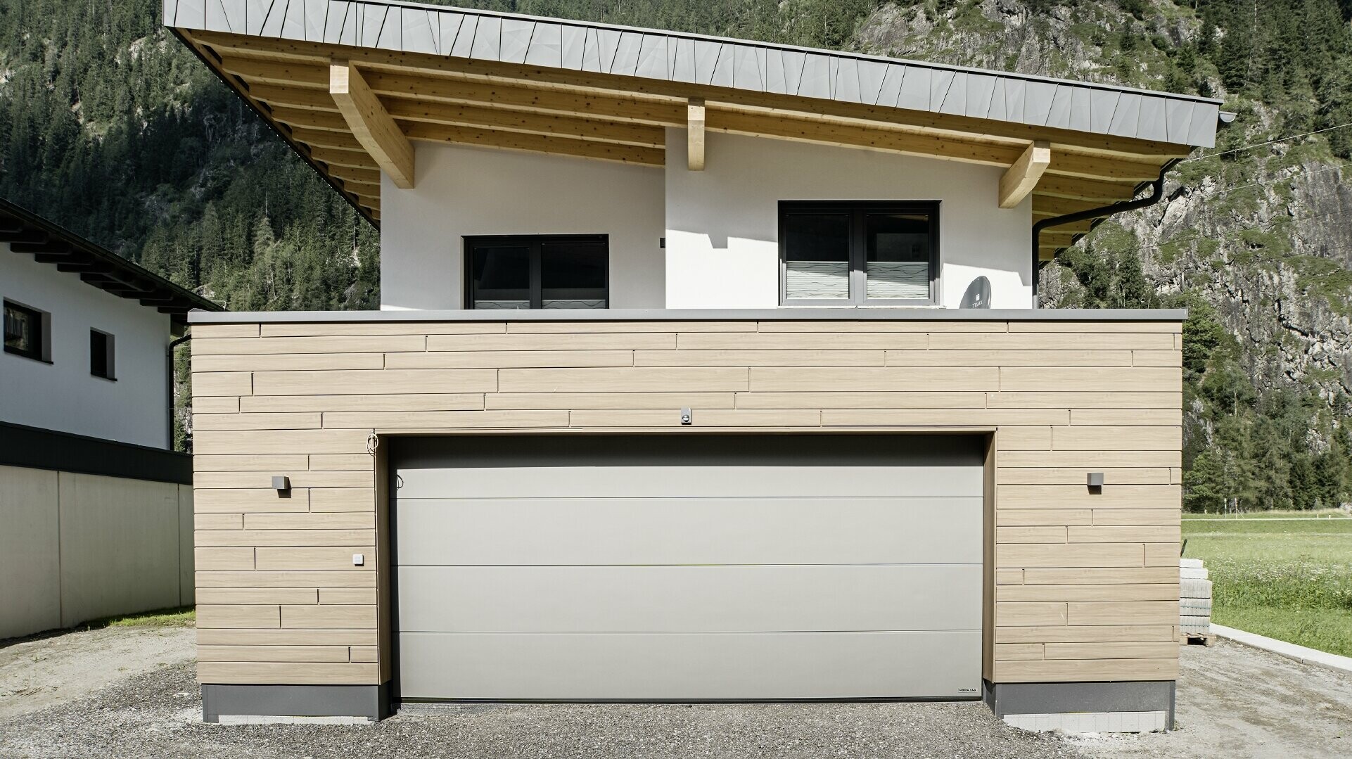 Modernt nybygge med pulpettak och speciell beklädnad på hängskivan, Garage med platt tak och med aluminiumfasad i valnötsbrun kulör från PREFA. Sidings är monterad horisontell och med olika byggbredder.