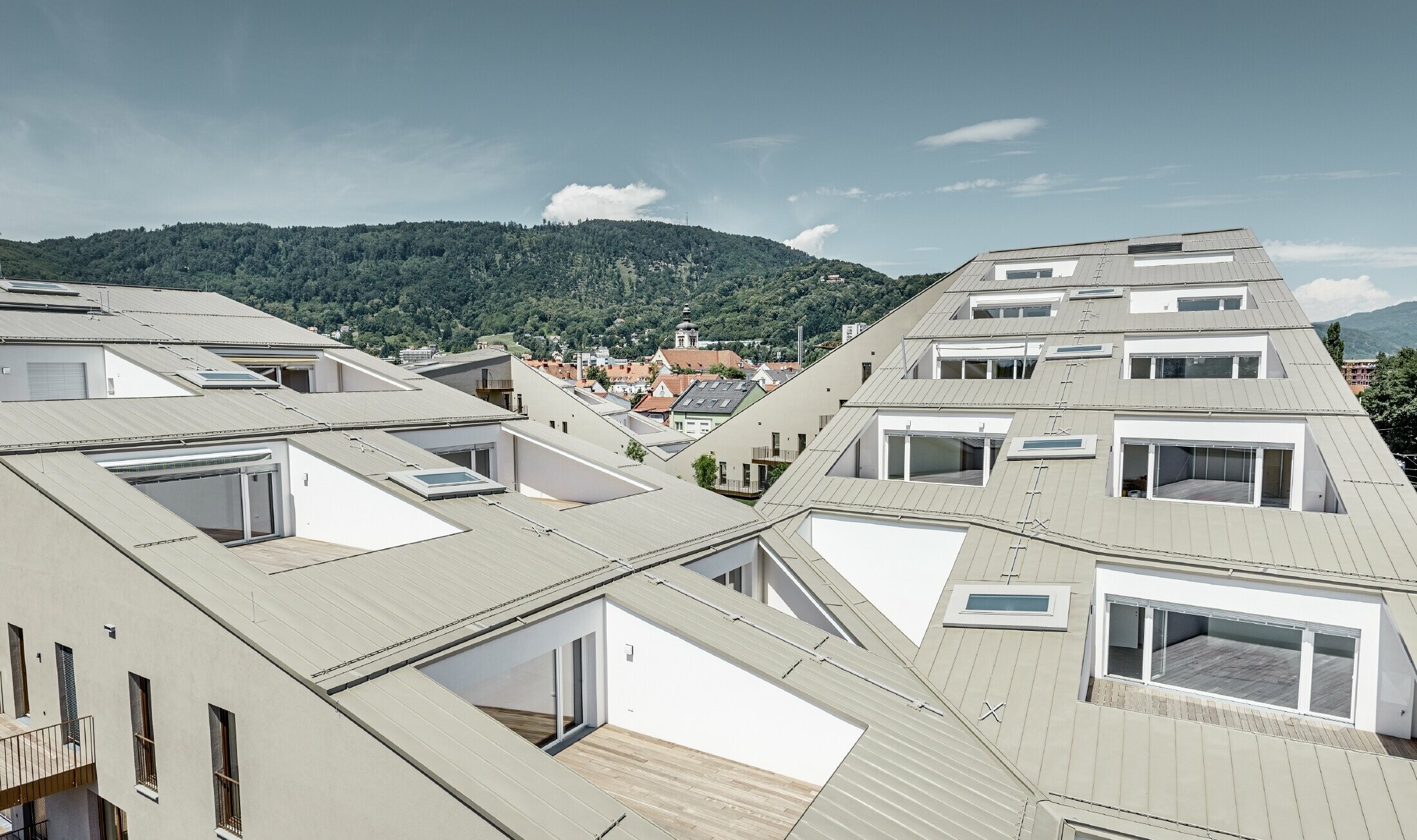 långsträckt bostadsbyggnad i Graz med plana takytor och integrerade terrasser och generösa fönster med ett prefalztak i specialfärgen bronsmetallic