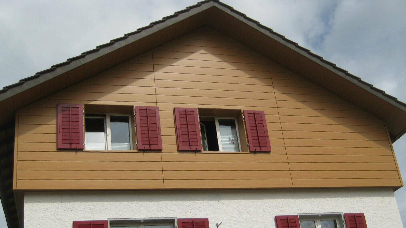 Husfasad i träutseende med PREFA sidings placerade horisontellt, fönster med röda fönsterluckor