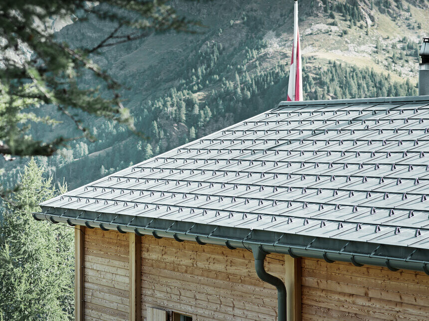 Schweizisk stuga täckt med PREFA takplatta och PREFA hängränna som är fäst med överbygel.