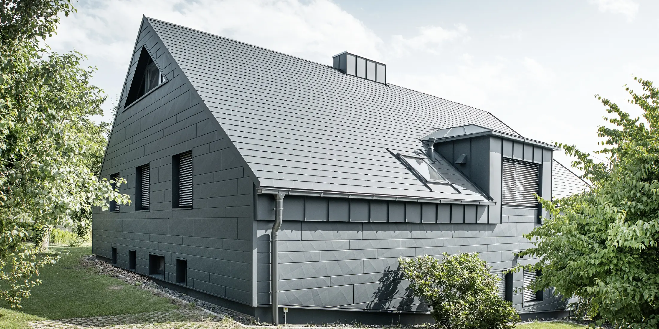 Stor villa med sadeltak och många fönster. Hela huset har klätts med en aluminiumhölje i antracit, på taket har PREFA aluminiumtakspån använts och på fasaden Fasadpanel.X i antracit.