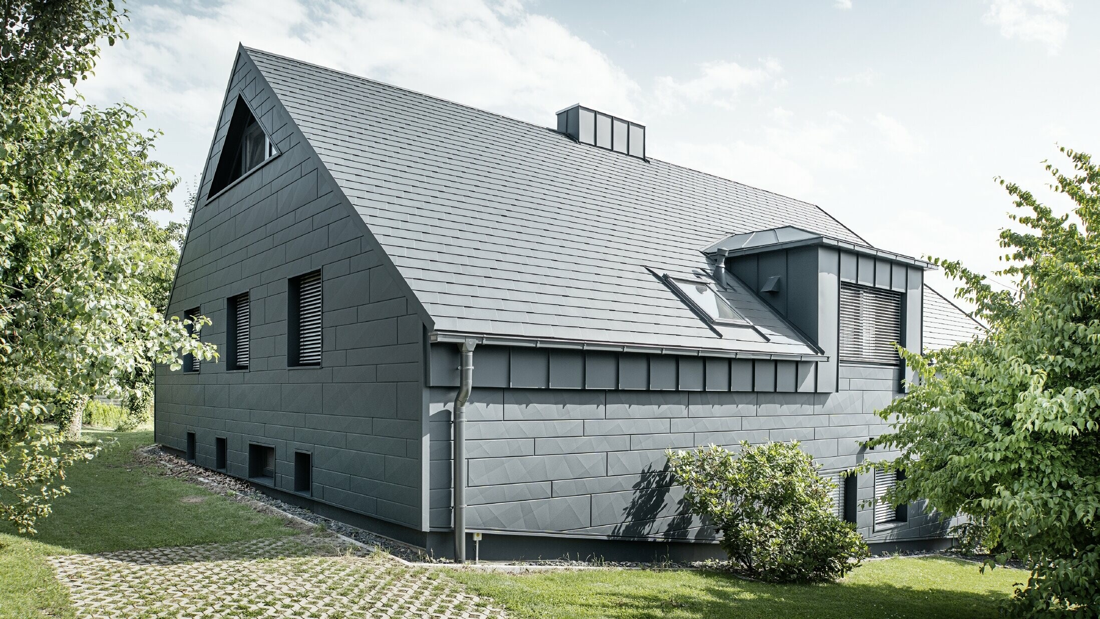 Stor villa med sadeltak och många fönster. Hela huset har klätts med en aluminiumhölje i antracit, på taket har PREFA aluminiumtakspån använts och på fasaden Fasadpanel.X i antracit.