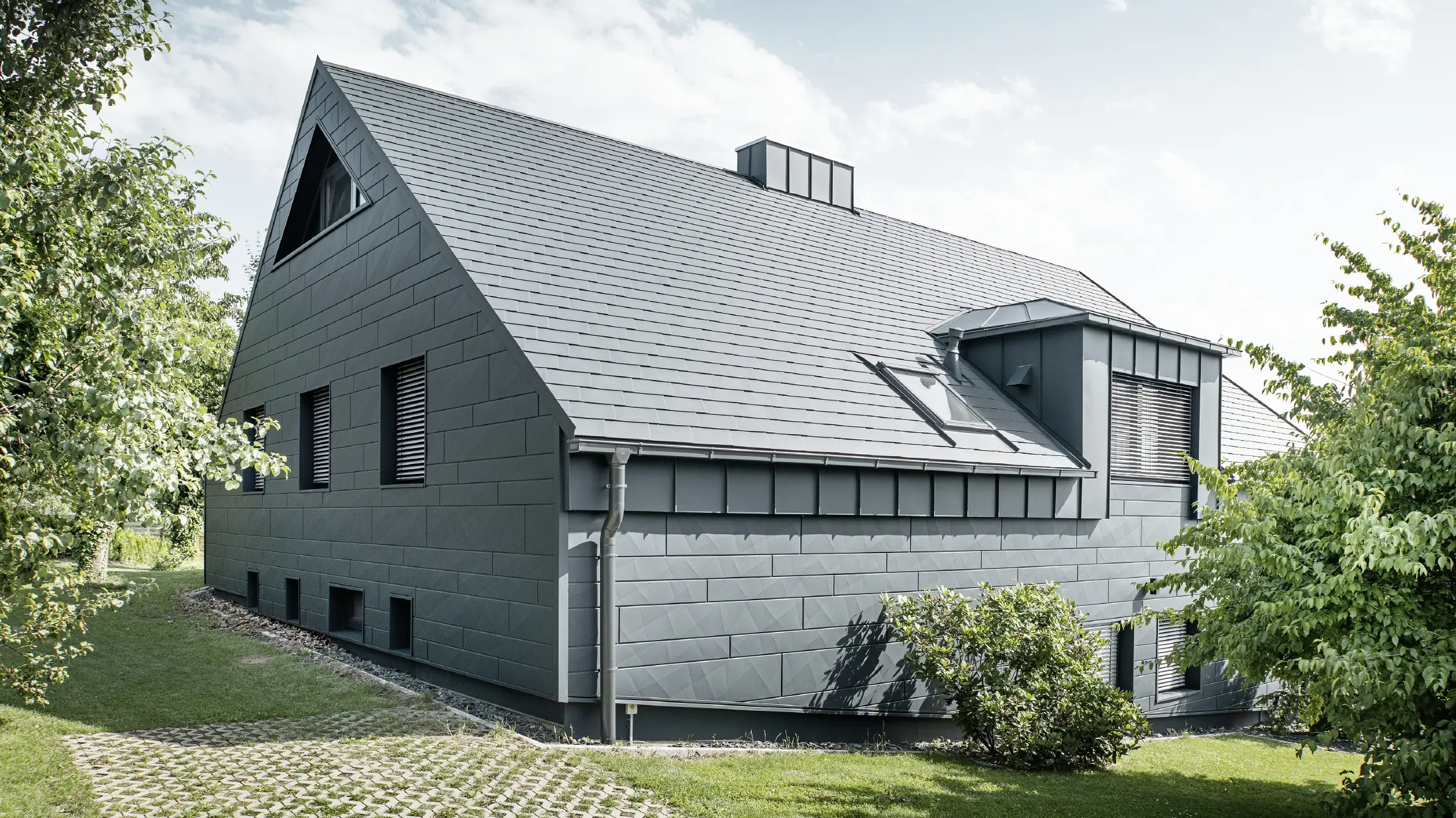 Stor villa med sadeltak och många fönster. Hela huset har klätts med en aluminiumhölje i antracit, på taket har PREFA aluminiumtakspån använts och på fasaden Fasadpanel.X i antracit.