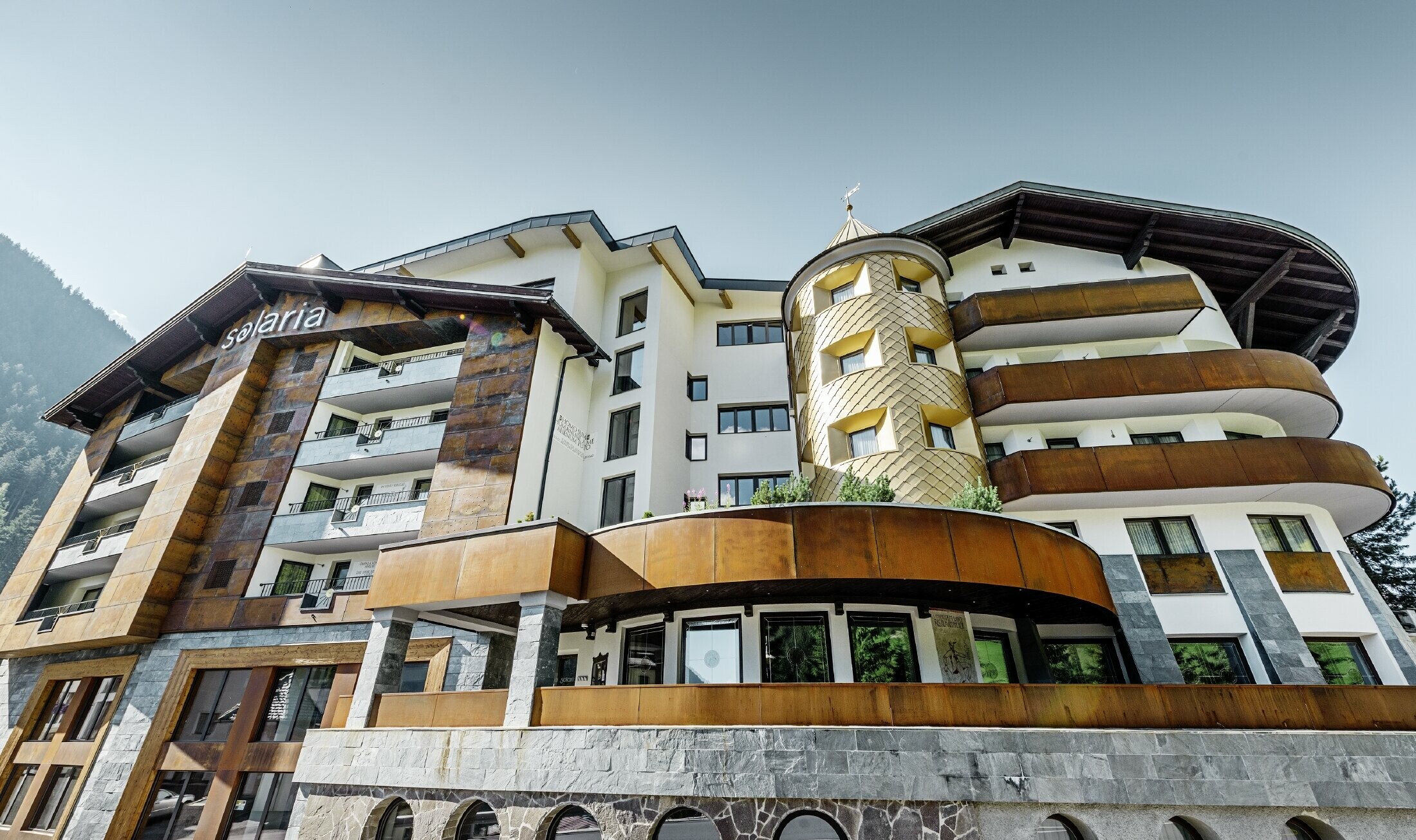 traditionellt hotell i Ischgl med träbalkonger och träfasad och ett torn med guldfärgade aluminiumromber från PREFA