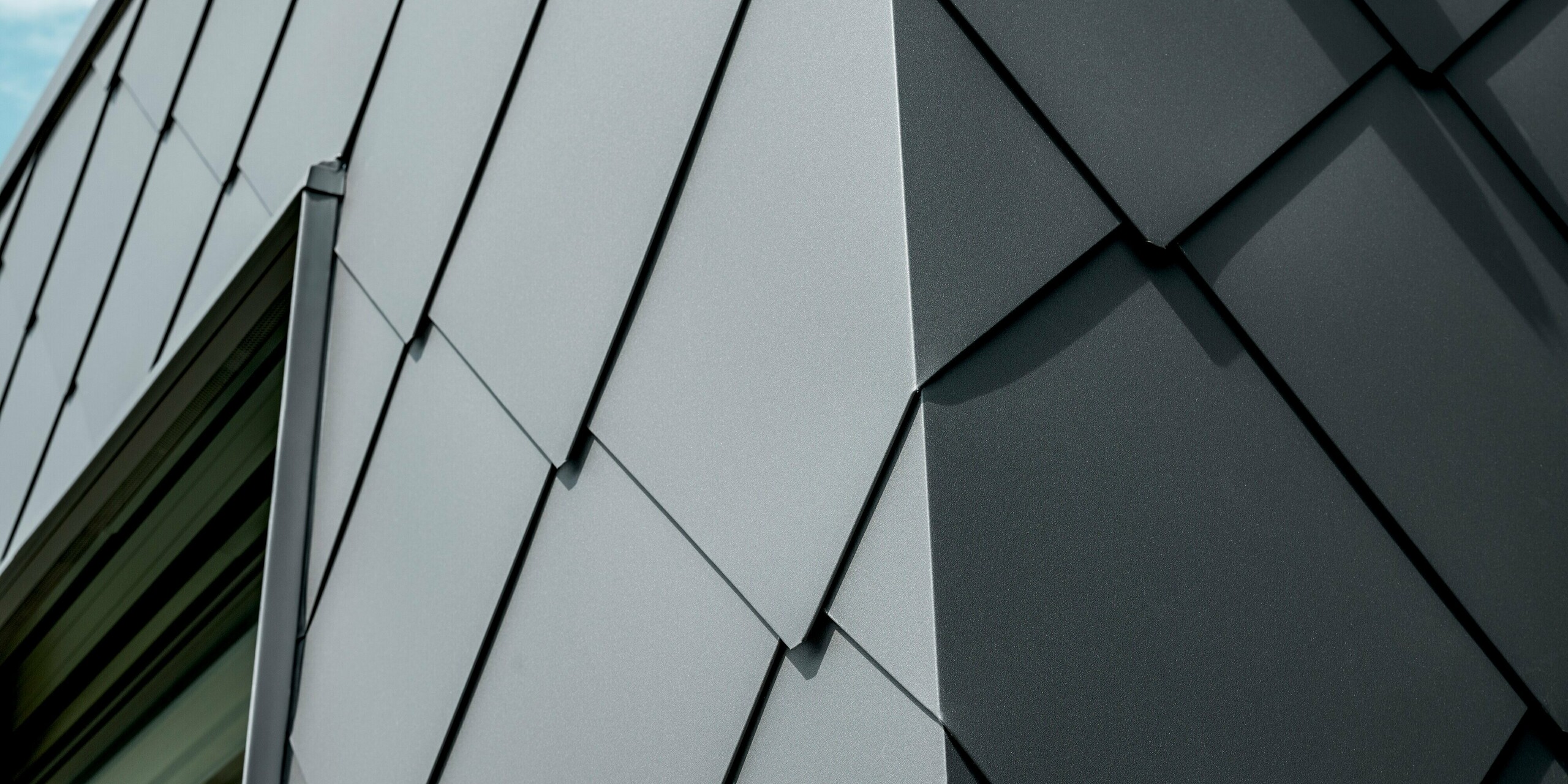 Detailaufnahme der PREFA Dach- und Wandrauten 44 × 44 in P.10 Dunkelgrau am Einfamilienhaus in Trnava‑Modranka. Das Bild zeigt die präzise verlegte Rautenstruktur, deren saubere Linien und Kanten das hochwertige Aluminium besonders hervorheben. Die matte Oberfläche sorgt für elegante Lichtreflexe und verleiht der Fassade eine moderne, technische Anmutung. Die langlebigen PREFA Aluminiumprodukte bieten maximale Witterungsbeständigkeit, Stabilität und ein durchgehend einheitliches Erscheinungsbild für eine markante, zeitlose Architektur.