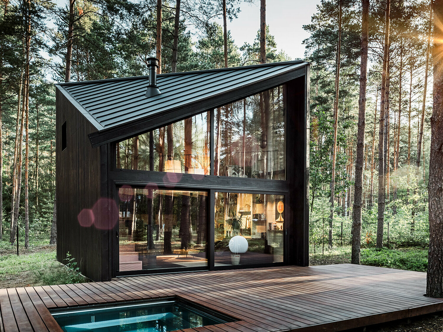 Seitenansicht eines Ferienhauses mit schrägem Prefalz-Dach. Die umgebende Natur spiegelt sich im verglasten Bereich wider.