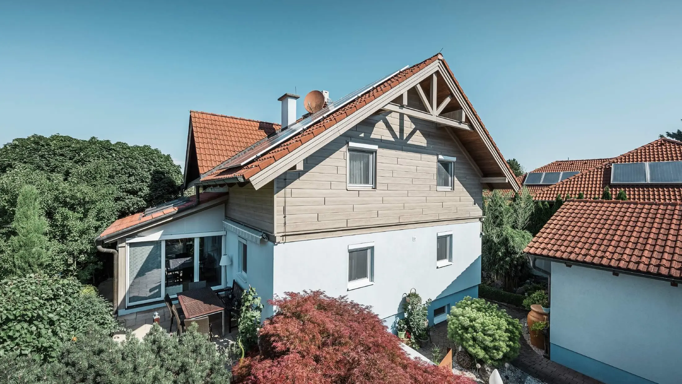 Fasaden av en villa som på övervåningen klätts med fasadpanel av trälook i färgen beige-grå ek
