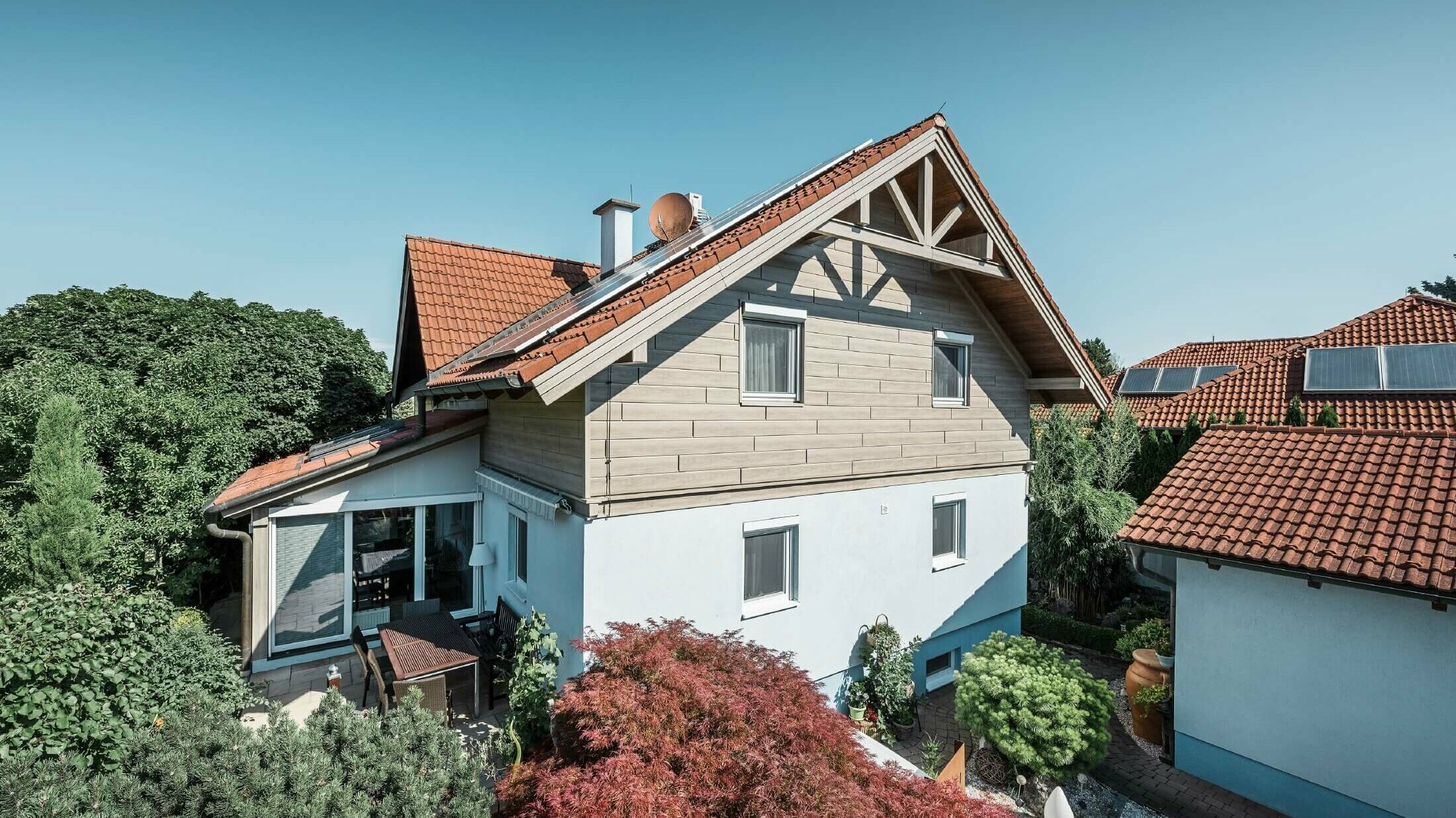 Fasaden av en villa som på övervåningen klätts med fasadpanel av trälook i färgen beige-grå ek