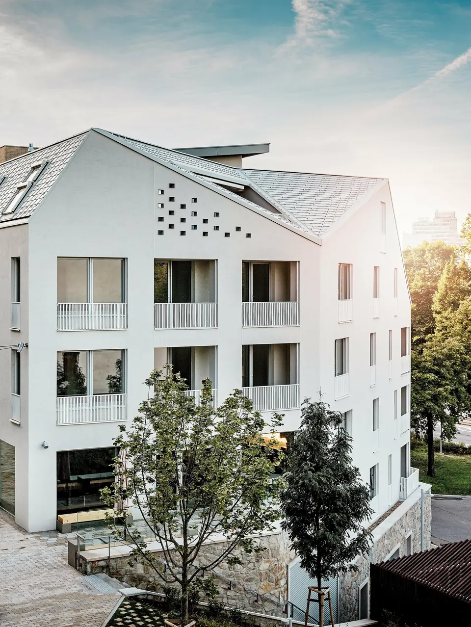 Modernes Wohnquartier Vydrica in Bratislava mit klarer Architektursprache und ruhiger Gassenatmosphäre: Die steil geneigten Satteldächer mit markanten Dachfenstern sind mit PREFA Aluminium Dachschindeln in P.10 Prefaweiß, Bronze und P.10 Sandbraun gedeckt und bilden einen eleganten Eyecatcher im Sonnenlicht. Die präzise ausgeführten Linien und homogenen Flächen unterstreichen die hochwertige Gestaltung. PREFA Aluminium überzeugt durch Langlebigkeit, geringes Gewicht und hohe Witterungsbeständigkeit – ideal für komplexe Dachformen und eine nachhaltige, wartungsarme Gebäudehülle.