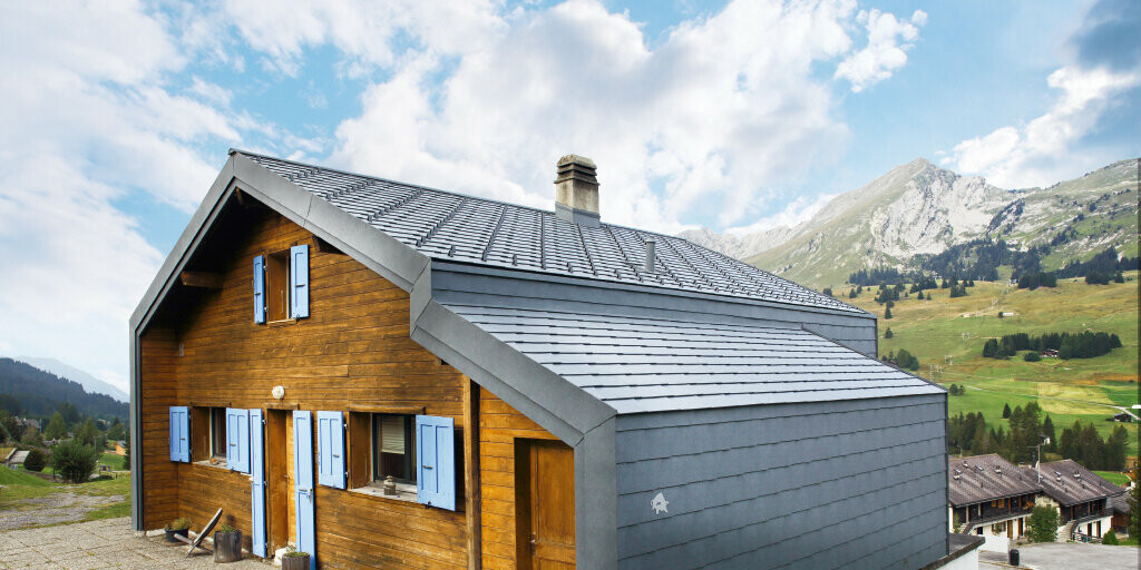 Haus i de schweiziska bergen med träfasad i kombination med PREFA tak- och väggromb i stengrå