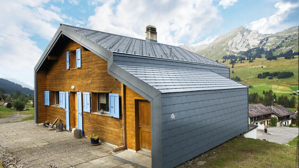 Haus i de schweiziska bergen med träfasad i kombination med PREFA tak- och väggromb i stengrå