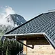 PREFA takplatta i alpin insats – Takplatta i antracit lagt på fjällstuga i Lech am Arlberg med berg i bakgrunden. PREFA takränna i antracit; träfasad
