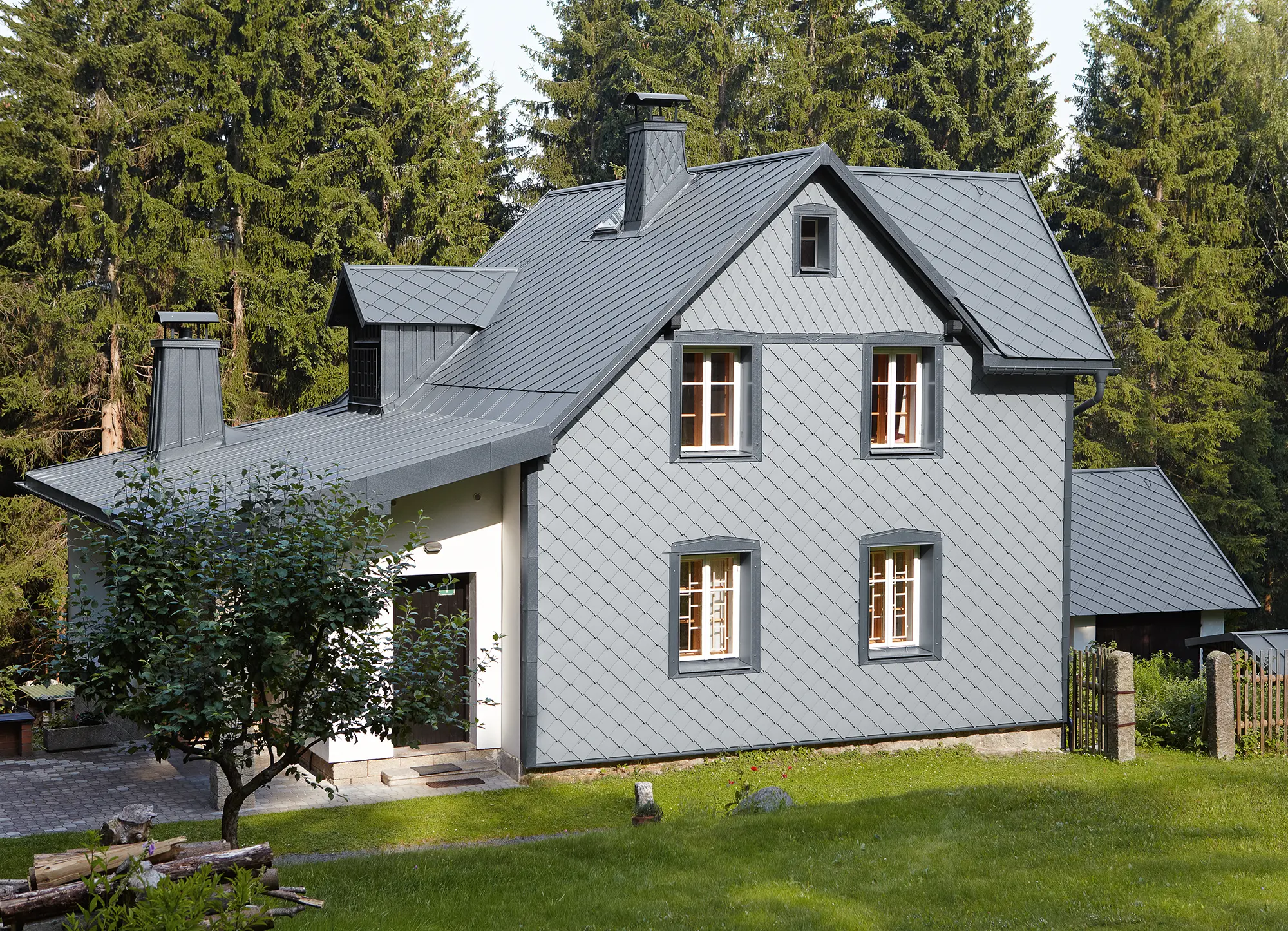 Enfamiljshus i skogsområde med väderbeständig PREFA aluminiumfasad i ljusgrå.
