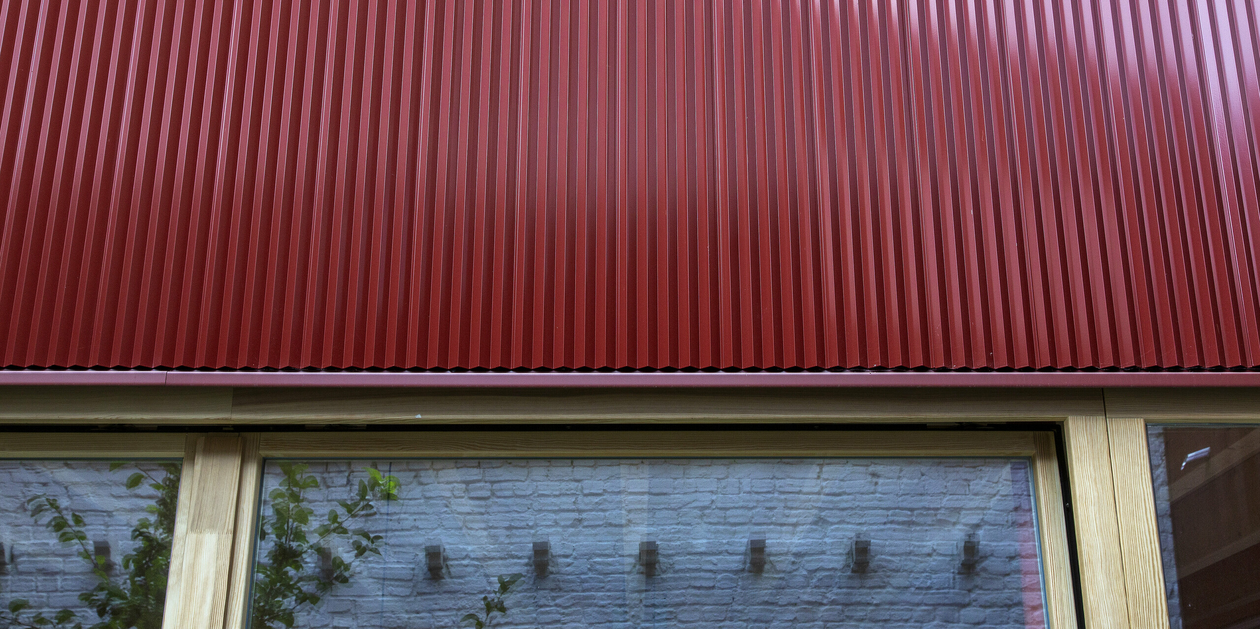 Nahaufnahme des PREFA Zackenprofils in der Farbe Oxydrot über einem großen Holzfenster: Die präzise Verarbeitung und die vertikale Struktur des stranggepressten Aluminiums sorgen für ein markantes, modernes Fassadenbild. Das langlebige Blechprofil ist witterungsbeständig, formstabil und verleiht dem Gebäude einen hochwertigen architektonischen Akzent.