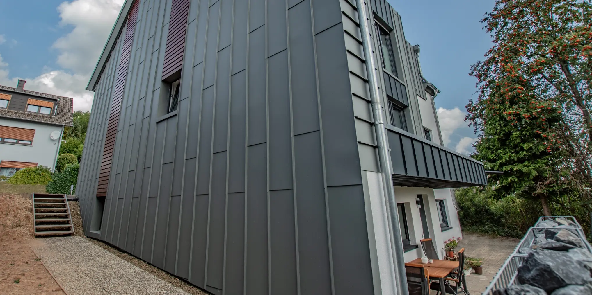 Fasaddesign med lodrätt stående vinkelfals i ljusgrått och vågrätt liggande fasadpaneler i mörk träimitation. Hela fasaden tillverkades av aluminium från PREFA.