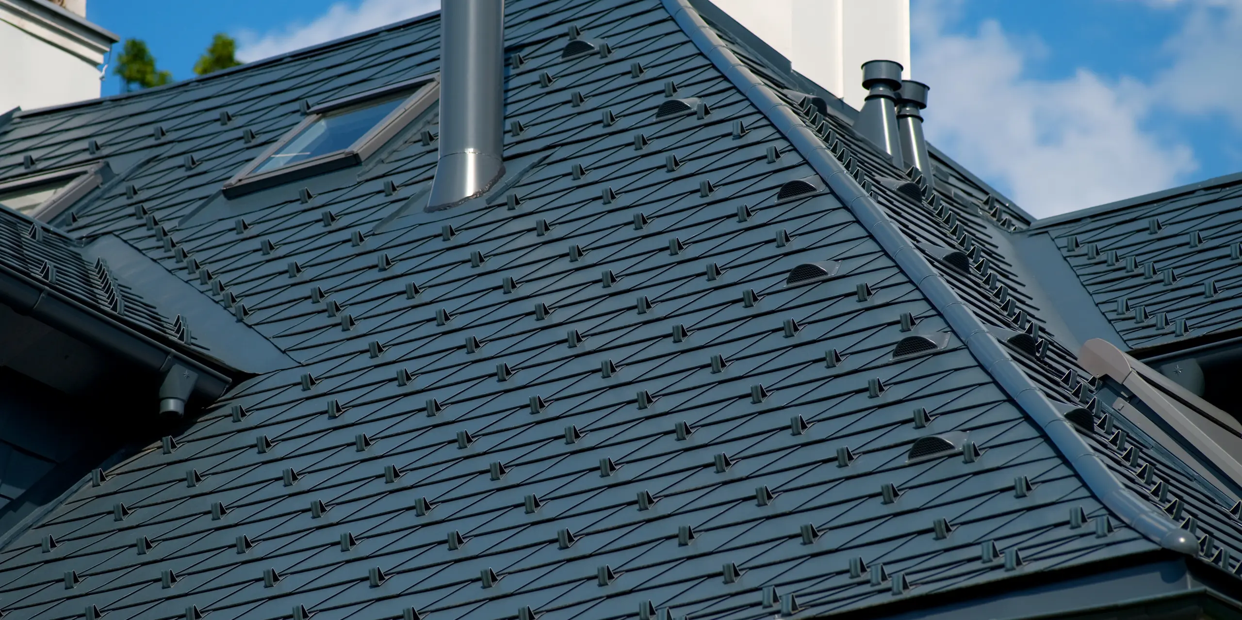 Nahaufnahme des aufwendig gestalteten Villendachs in Bad Aussee mit PREFA Dachschindeln aus Aluminium in P.10 Anthrazit. Die präzise verlegte Dachfläche mit Schneefangsystem, Dachfenster und markanten Dachdetails zeigt die hohe Verarbeitungsqualität. Die langlebigen PREFA Dachschindeln überzeugen durch ihre Widerstandsfähigkeit, Wetterbeständigkeit und ihre elegante, zeitlose Optik.