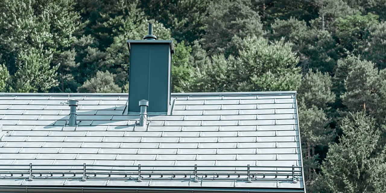 Detaljbild på sadeltaket, täckt med PREFA takplatta R.16 i stengrått med snörassystem, skorstensinfattning, takrännor och ventilationsrör, även dessa från PREFA