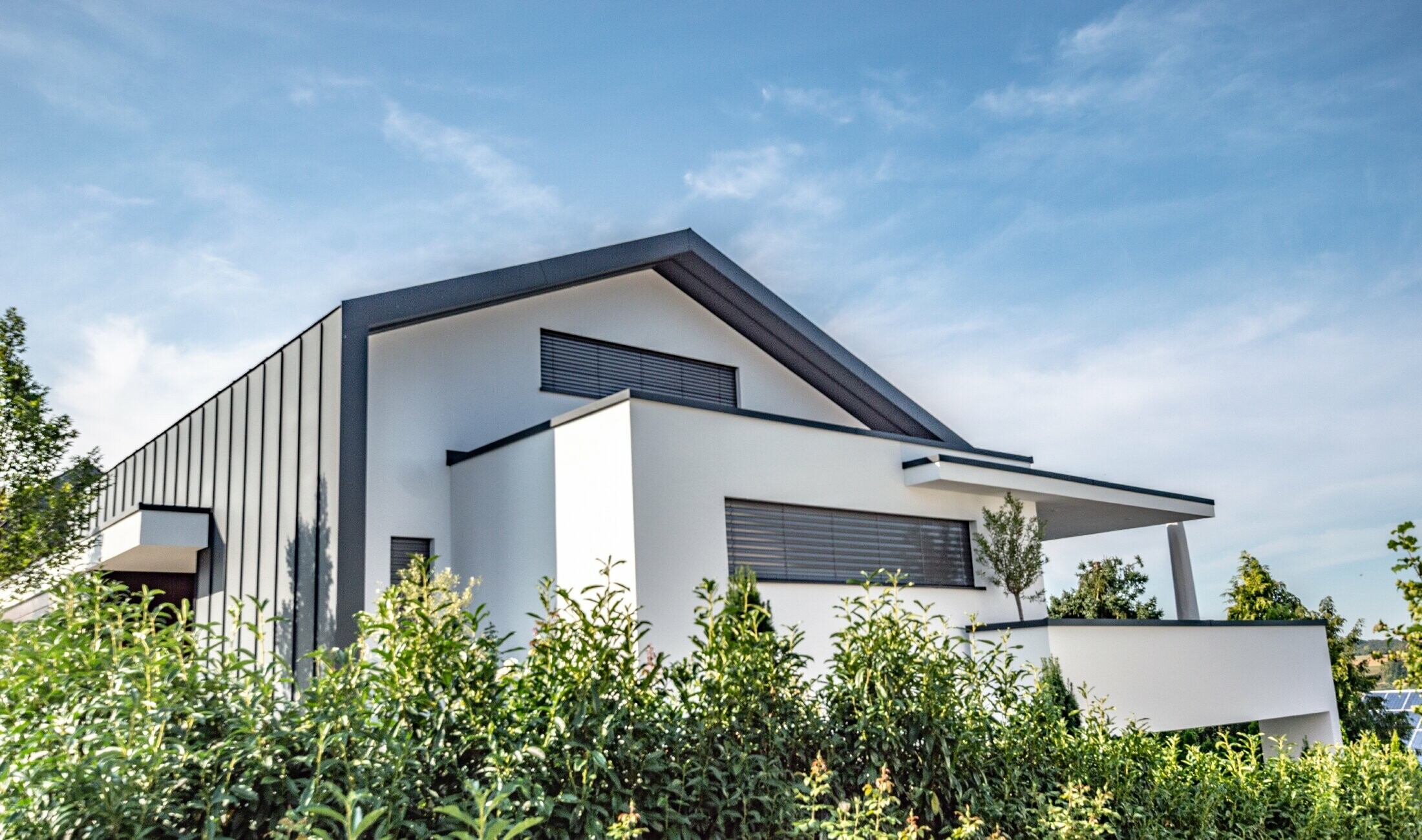 På detta moderna familjehus fortsätter takbeläggningen som stående vinkelfals visuellt från fasadbeläggningen. Färgen på PREFA-materialet är antracitgrått.