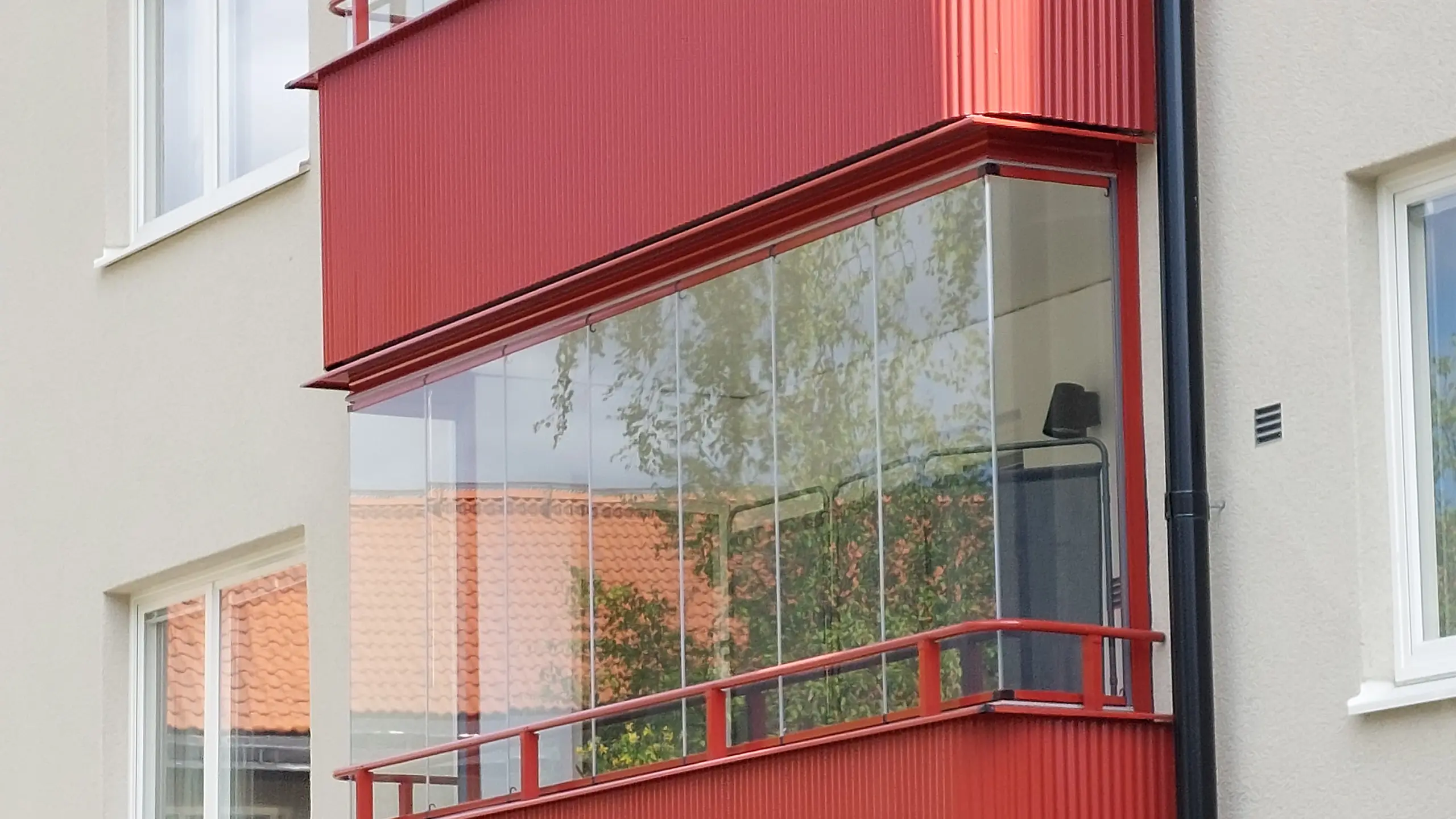 Två balkonger på ett bostadshus med gnejsröd Alustucco-beklädnad och inglasning, som tydligt kontrasterar mot den ljusa fasaden.
