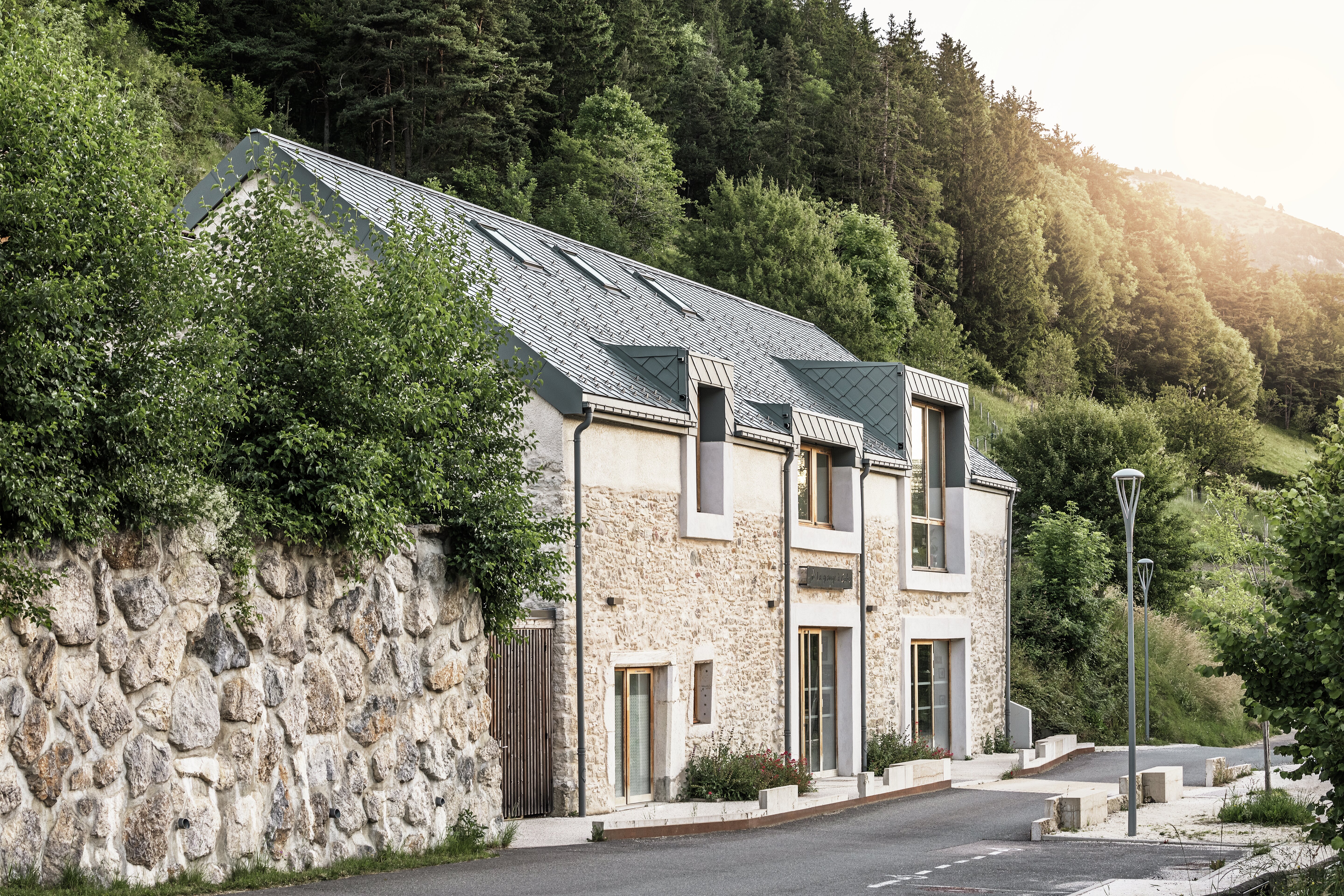 Die renovierte Scheune „La Grange à Gaby“ in Engins, Frankreich, vereint traditionelles Steinmauerwerk mit einem modernen PREFA-Aluminiumdach aus 29 × 29 cm großen Rauten. Die Renovierung verbindet den historischen Baustil mit zeitgenössischer Architektur und nachhaltigen Materialien.