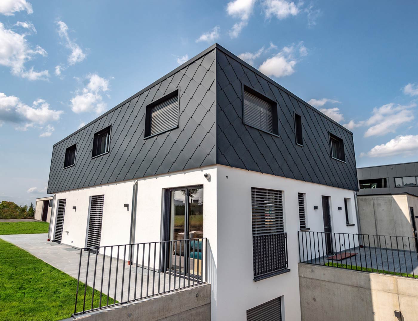 PREFA väggromb 44× 44 antracit referens Modern nybyggnad med platt tak - fasaden på övervåningen är klädd med PREFA väggromber 44 × 44 i antracit. Den nedre fasaddelen är putsad vit.
